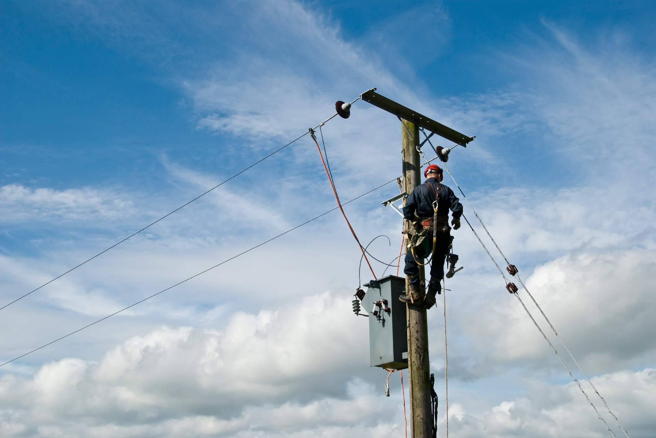 An unrecognisable utility workman carries out repairs on a transformer connected to an 11000 volt power line.
